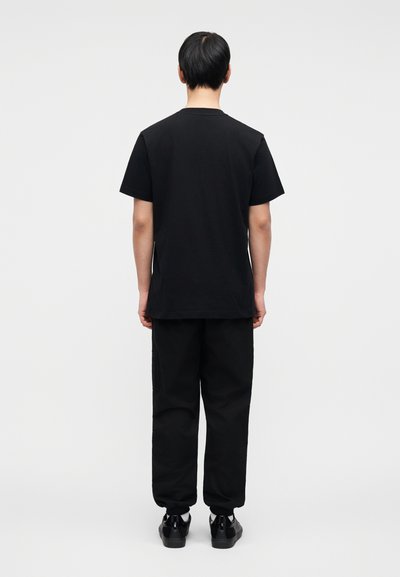 Μαύρο βαμβακερό μπλουζάκι με στρογγυλή λαιμόκοψη, συνδυασμένο με μαύρο παντελόνι. Το σύνολο έχει άνετη εφαρμογή και μινιμαλιστικό σχεδιασμό.