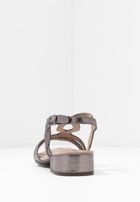 Sandale grise métallique avec une bride au niveau de la cheville, dotée d'un petit talon carré et d'une texture lisse. Détail de boucle sur la bride, design ouvert.