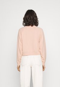 Ljusrosa kort sweatshirt med raglanärmar, ribbade muddar och nederkant. Baksidan har en slät yta och kombineras med vita vida byxor.