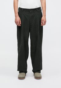 Tamsiai žalios spalvos kordūro kelnės su plačiomis kojomis, turinčios priekinę klostę ir mygtuko uždarymą. Audinys atrodo tekstūruotas, su grioveliais.