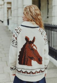 Knit sweater with a horse design, featuring cream, brown, and navy colors. Striped collar, patterned accents, and thick texture.