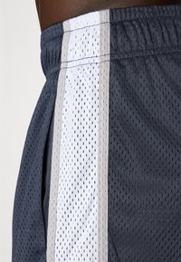 Mørkegrå treningsshorts med et hvitt og grått mesh-panel langs siden, med små perforeringer og elastisk midjebånd.