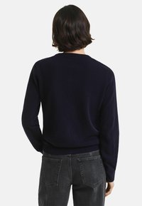 Mörkblå tröja i mjukt tyg, med rund halsringning och långa ärmar, samt en figurnära ribbad fåll och minimalistisk design.