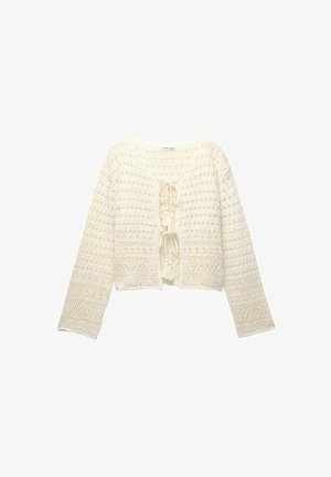 Pleteni kardigan v off-white barvi s skrajšano zasnovo, odprtim sprednjim delom, vezanjem s pomponi in dolgimi rokavi, ki vsebujejo teksturirane vzorce.