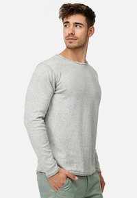 Jasnoszara, długorękawowa koszulka typu crew neck, wykonana z miękkiej, teksturowanej tkaniny z subtelnym wzorem kropek oraz wyszywanym detalem przy dekolcie.