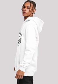 Hvid hættetrøje med en frontlomme, prydet med et sort grafisk print. Stoffet ser blødt ud med ribbede manchetter og en afslappet pasform.