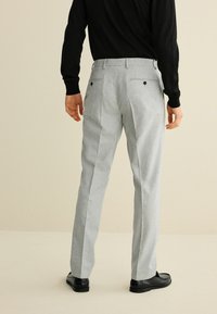 Hellgraue, maßgeschneiderte Hose mit einer glatten Textur, ausgestattet mit zwei Gesäßtaschen und einer geraden Silhouette, kombiniert mit einem schwarzen Langarmhemd.