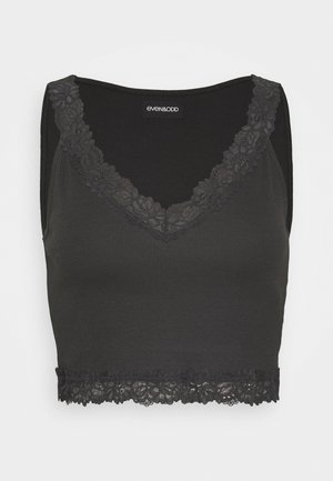 Zwarte cropped tanktop gemaakt van ribstof. Heeft een kantafwerking rond de halslijn en onderkant, met een aansluitend ontwerp.