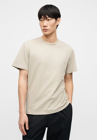 Μπεζ κοντομάνικη μπλούζα από βαμβάκι, με κλασικό στρογγυλό λαιμό και άνετη γραμμή. Ομαλή υφή χωρίς σχέδια.