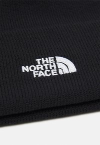 Black knitted beanie with ribbed texture, featuring a white embroidered logo of "THE NORTH FACE" and a curved design element.