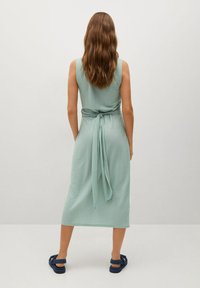 Robe sans manches vert menthe avec une taille à lien, longueur genou, fabriquée en tissu léger ; assortie à des sandales bleues.