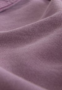 Ljuslila tyg med en strukturerad yta, som har fina, regelbundna ribbor. Materialet ser mjukt ut och faller elegant.