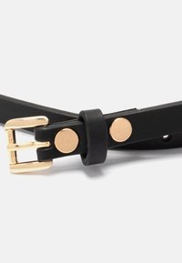 Cinturón de cuero negro con hebilla de metal dorado, con un detalle de tachuela redonda y múltiples agujeros de ajuste para el tamaño. Textura suave en toda su superficie.