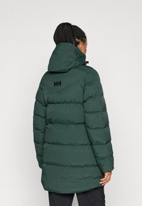 Geacă puf verde cu glugă, cu un design matlasat, logo negru pe spate și o croială ușor mai lungă pentru mai mult confort.