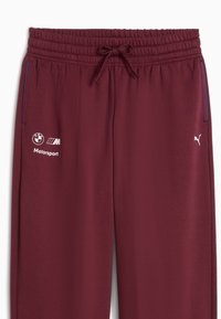 Burgundské tepláky s elastickým pasem a šňůrkou. Obsahují bílé logo Puma a branding BMW Motorsport. Modré boční detaily. Hladká textura.