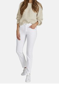 Jeans blancos de pierna recta con una cintura alta que presentan una textura suave y un cierre de botón metálico clásico. Combinados con un suéter de punto beige.