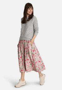 Hellgrauer Pullover mit strukturiertem Strick, kombiniert mit einem langen Rock mit Blumenmuster in Pink- und Grüntönen, getragen mit beigen Sneakers.