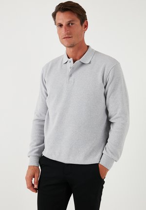 Light grey long-sleeve polo shirt with a collar, three buttons, and ribbed cuffs. Smooth texture with a casual fit, paired with black pants.