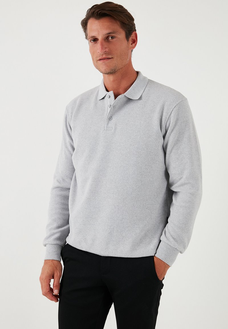 Camisa polo de manga larga gris claro con collar, tres botones y puños acanalados. Textura suave con un ajuste casual, combinada con pantalones negros.