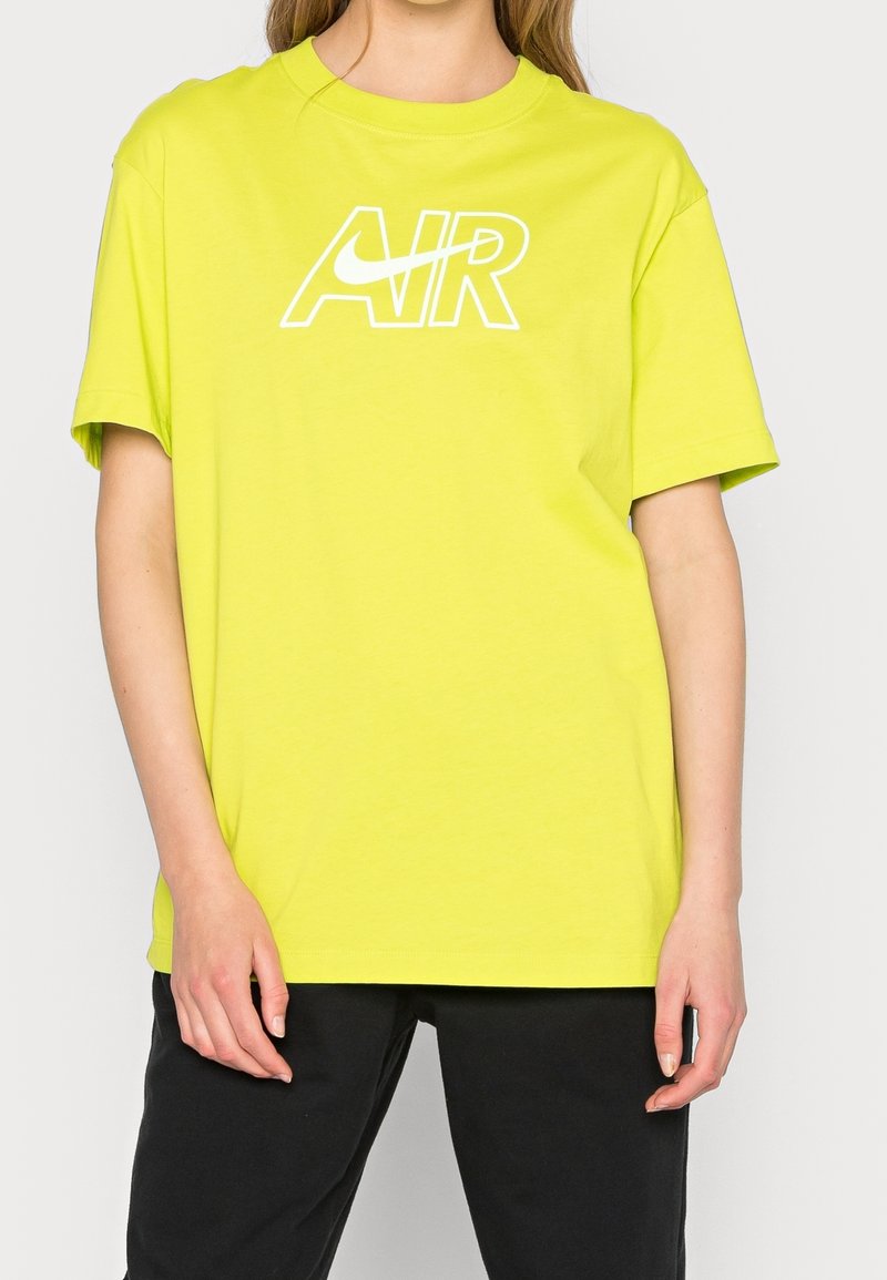 Jasnożółta koszulka Nike z białą grafiką "AIR" z przodu, krótkie rękawy, okrągły dekolt i luźny fason.