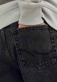 Grå denimjeans med en synlig bakficka som har en subtil sömdesign och en ljusgrå ribbad midja.