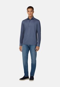 Navy poloshirt met lange mouwen en drie knopen, gecombineerd met lichtblauwe spijkerbroek en donkere instappers. Soepele stofstructuur.