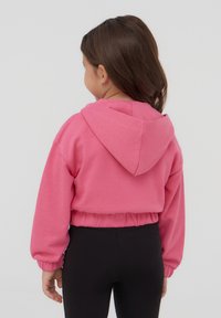Felpa cropped rosa con cappuccio, polsini e bordo a coste, abbinata a leggins neri. Texture liscia, design casual.