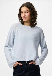 Ljusblå tröja i mjuk stickad kvalitet, med rund hals, vågig nederkant och lång ärm, bärs tillsammans med mörka jeans.