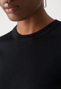 Svart ribbad topp med rund halsringning, som visar en mjuk textur och en nära passform. Utmärkande drag inkluderar en subtil lyster och ren sömnad.