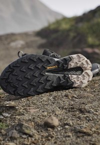 Gros plan de la semelle d'une chaussure de randonnée noire et beige avec un profond motif de la bande de roulement et le logo Continental sur un terrain rocheux en plein air.