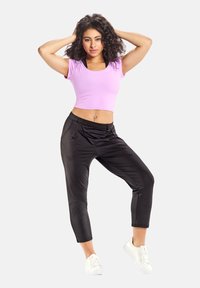 Top corto rosa chiaro e pantaloni cropped neri in satin con tasche, abbinati a sneakers bianche. Texture liscia e design aderente.