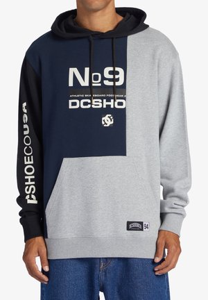 Sudadera gris y azul marino con un bolsillo frontal, mangas largas y capucha con cordón. Presenta logotipos y números impresos en negrita en el pecho y la manga.