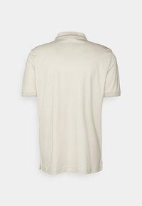 Polo shirt in off-white met een zachte textuur, korte mouwen en een kraag. Heeft zijsplitten aan de onderkant voor meer bewegingsvrijheid.