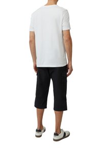 Witte katoenen T-shirt met korte mouwen, gecombineerd met knielange zwarte cargo shorts en witte sneakers met grijze accenten.