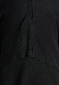 Black fabric close-up features a smooth texture with visible stitching lines, highlighting the garment's design and seam details.