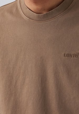 Ruskea puuvillainen crewneck T-paita, jossa on ribattu kaula-aukko ja brodeerattu Levi's-logo sameassa värissä, sileällä ja pehmeällä pinnalla.