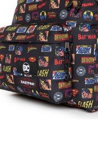Mochila de tela negra con gráficos de personajes de cómic, incluyendo a Batman y Wonder Woman, con los logotipos de Eastpak y DC. Detalle de bolsillo con cremallera.