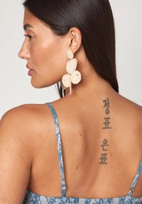 Robe en tissu bleu tissé avec des bretelles fines, arborant un motif floral. Le modèle porte de grandes boucles d'oreilles texturées. Un tatouage dans le dos avec des caractères coréens est visible.