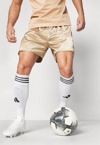 Beige satinsockor med sidoklipp, kombinerat med vita strumpor med tre svarta ränder och en texturerad svart och vit fotboll.