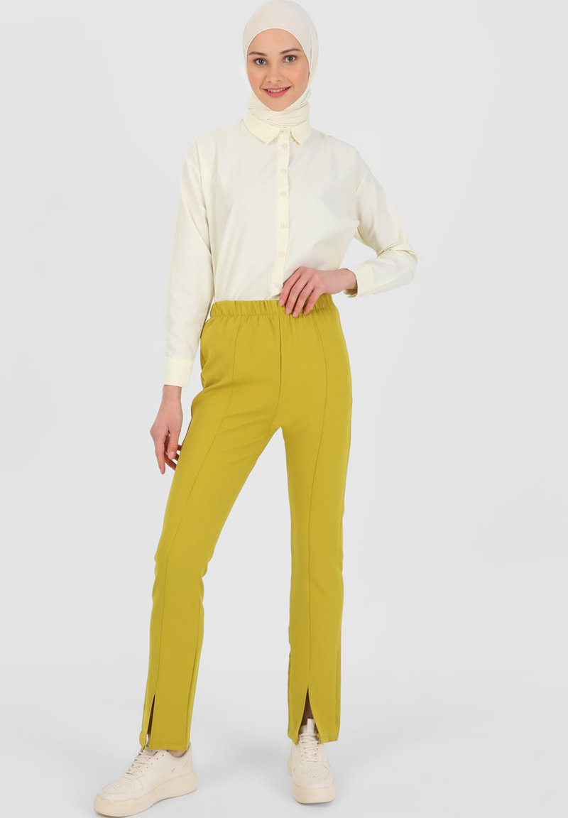 Biała bluzka z długim rękawem, zapinana na guziki, w połączeniu z żółtymi spodniami ze prostymi nogawkami, posiadającymi elastyczny pas i boczne rozporki. Białe sneakersy.