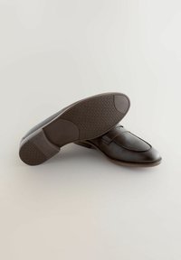 Mocasines de cuero marrón con punta redonda, detalle de costura de silla y suela de goma texturizada con patrón geométrico.