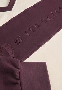 Bordoopunane puuvillane särk, millel on tekstureeritud kude, selgelt nähtava beeži triibuga ja tikandiga "BY TED BAKER" detail. Volangiga varrukate aksendid.