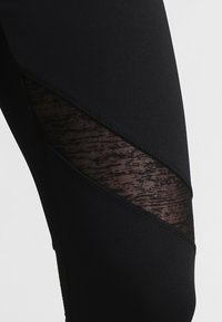 Black athletic leggings featuring sheer mesh panels with a textured pattern and diagonal cutouts, made from stretchy, breathable material.