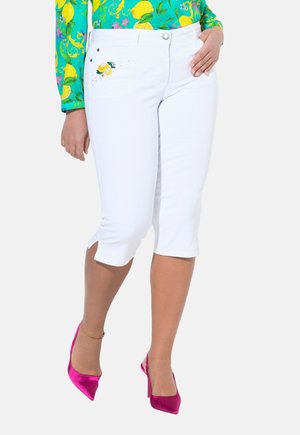 Weiße Capri-Hosen mit seitlichem Schlitz und Zitronenstickerei auf der Vordertasche, kombiniert mit pinken Satin-Pumps.