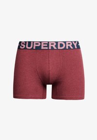 Czerwone bawełniane szorty z dopasowanym krojem i granatową gumką w talii, na której widnieje biały napis "SUPERDRY". Miękka tekstura.