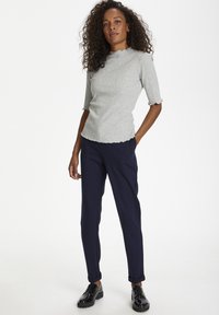 Grå ribbad topp med vågiga kanter, korta ärmar, ihop med marinblå byxor och svarta snörskor. Enkel, figurnära design.