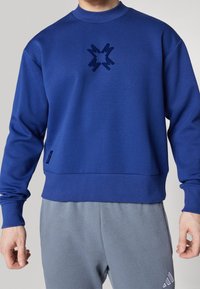 Felpa blu con collo alto, tessuto morbido e logo frontale a forma di stella. Polsini e orlo a costine, abbinata a pantaloni grigi.