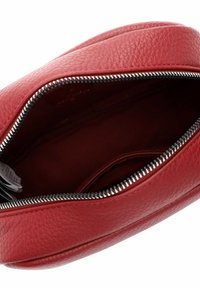 Sacca in pelle rossa con una texture granulosa, dotata di una zip in argento. L'interno presenta una fodera scura e un piccolo scomparto.