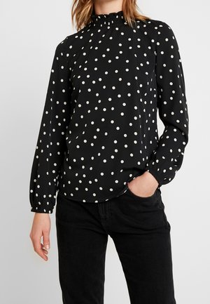 Blusa nera a maniche lunghe con pois bianchi, colletto alto con dettaglio arricciato e polsini elastici, realizzata in un tessuto leggero.