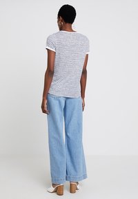 Camiseta de manga corta a rayas, hecha de una tela suave, combinada con unos pantalones vaqueros de mezclilla de tiro alto y pierna ancha en un tono azul claro. Calzado casual con tacones cuadrados.